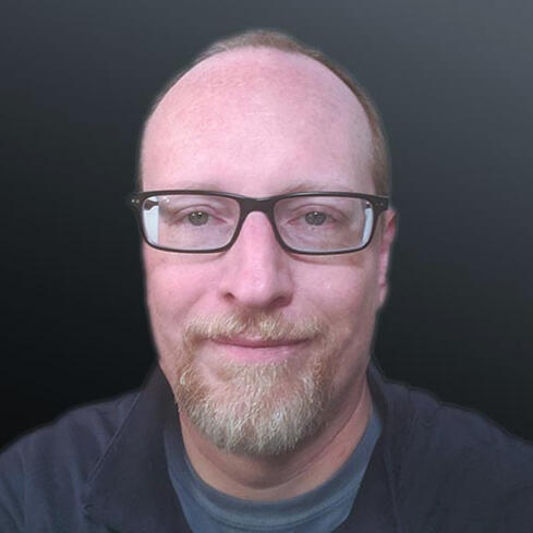 A man's face with a high forehead, dark glasses, and a reddish blonde turning white goatee.